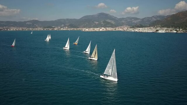 Aerial close view of the sailing boats regatta with city view behind. Drone moves forward