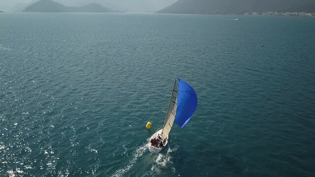 Aerial very close view of the sailing boat passing mark and take out spinnaker