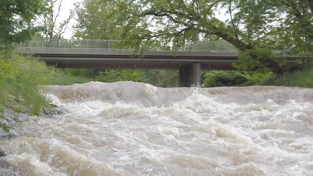 Slow motion of a highwater river with a bridge starting with close splashes
