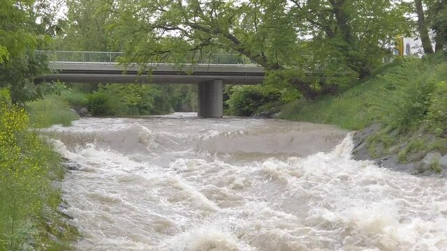 Slow motion of a muddy highwater river with a bridge, slowly tilting down