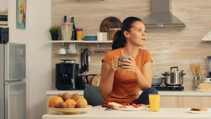 Woman drinking hot coffee at breakfast in kitchen and delicious food on table top. Lady ejoying a cup of coffee in the morning. Happy housewife relaxing and spoiling herself with a healthy meal alone