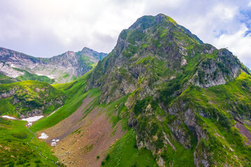 The top of a rocky mountain on a ridge with green meadows and snow, streams. Aerial drone view.