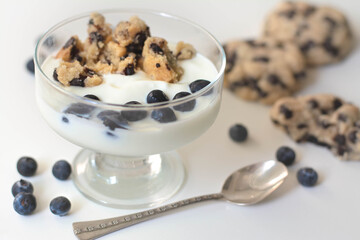 Cold parfait dessert with creamy yogurt, crumbled chocolate chip cookies and blueberries. White background.