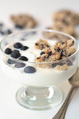 Cold parfait dessert with creamy yogurt, crumbled chocolate chip cookies and blueberries. White background.