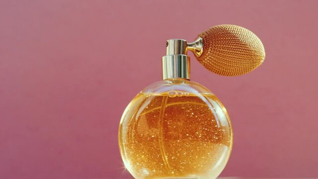 Luxury golden perfume bottle and shining light flares on pink background, glamorous fragrance scent as perfumery product for cosmetic and beauty brand, stock footage