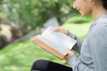 Pretty young woman reading bible in park. Reading abook.The concept of God's bible is based on faith and spirituality.