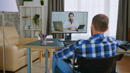 Obraz premium Disabled young man in wheelchair during a video call with his doctor.