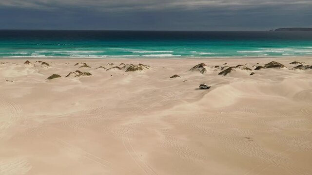 Isolated 4WD jeep facing the ocean before a thunderstorm. Wide aerial shot