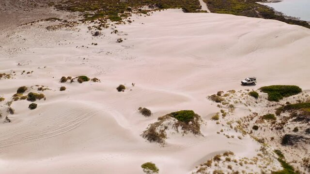 Aerial Tracking shot of a white jeep climbing over the sand dunes on the Australian coast