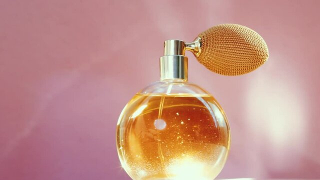 Luxury golden perfume bottle and shining light flares on pink background, glamorous fragrance scent as perfumery product for cosmetic and beauty brand, stock footage