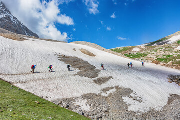 Idyllic summer landscape with hiking trail in snow mountains with trekkers.