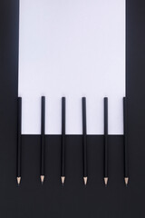 Obraz premium On a black table lie black pencils and white paper. Workplace. Flat lay. Business concept