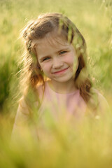 Naklejka na ściany i meble Portrait of a cute girl in a pink dress. Girl posing in a green wheat field.