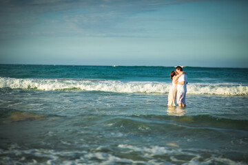 couple in white clothes in water on beach. 