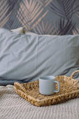 Fototapeta na wymiar Cup of tea on wicker stand on the bed linen in Scandinavian style. Cozy morning at home.