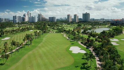 4K cinematic aerial of scenic Miami city skyline with ideal green golf course, tropical palm trees, modern apartment buildings on background, Florida, USA. Sunny summer day with clouds in blue sky