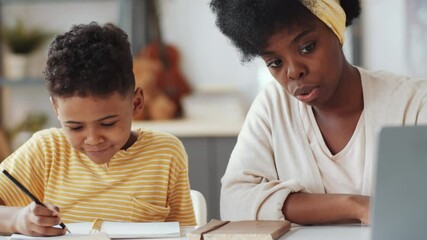 Close up shot of beautiful African American woman showing and explaining something on laptop screen while doing homework together with 7 years old son - Powered by Adobe