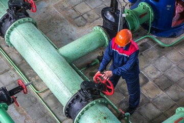 View from above of engineer in helmet working at water pump station.