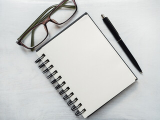 Blank notepad page, pen and glasses. Greeting card. Close-up, view from above, wooden surface. Concept of preparation for a professional holiday. Congratulations for relatives, friends and colleagues