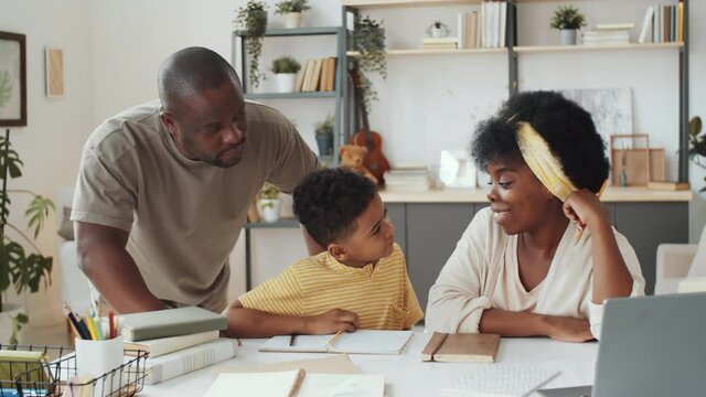 Little Afro-American boy doing homework with help of loving mother and dad while studying at home during lockdown