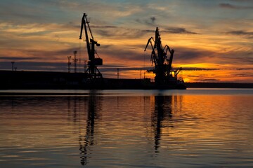 Obraz premium Black silhouettes of high cranes in sea cargo port and wonderful sunset. Arkhangelsk, Russia.
