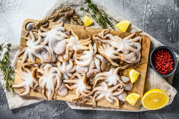 Fototapeta na wymiar Raw baby octopus with thyme and lemon in a wooden bowl. Organic seafood. Gray background. Top view