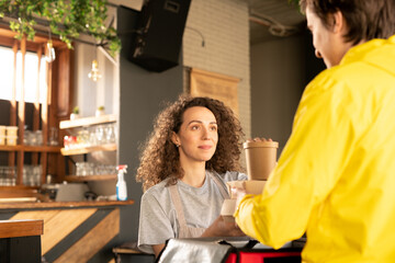 Content pretty waitress with curly hair giving packaged boxes to deliver boy for delivering to customer during coronavirus epidemic