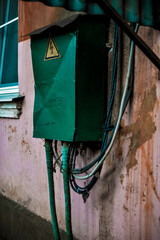 green electrical distribution box hanging on a ragged wall