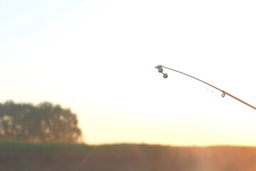 Fishing rod on sky background at beautiful sunset early morning on river. Background with wild nature in beautiful place at summer time. Silhouette of woodland forest.