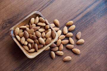 Almonds in small wooden bowl. Almonds laid freely on dark table. Row of bowls with almond nuts, top view. Peeled almond pattern