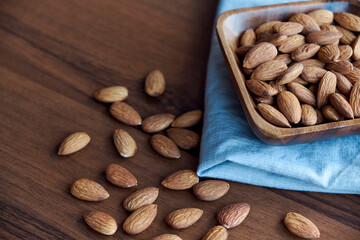 Almonds in small wooden bowl. Almonds laid freely on dark table. Row of bowls with almond nuts, top view. Peeled almond pattern