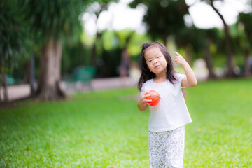 Happy Asian girl is playing a small orange ball. Child held a rubber ball in her hand and smiled...