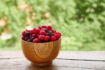 Wooden bowl of delicious red and black raspberries on a background of green foliage