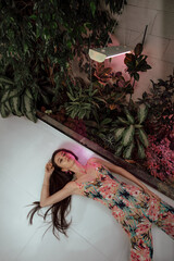 Attractive fashion model posing in a designer jumpsuit with a floral print lies on the floor in...