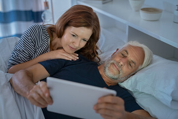 Mature sleepy couple using digital tablet at night
