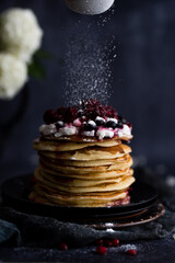 Stack of pancakes with sugar powder splashes on dark background table.