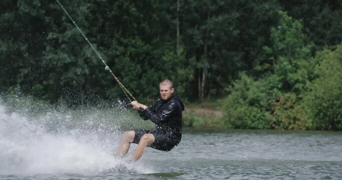 Wakeboarding in a lake near the forest, sportsman surfs on the water, ride on a wakeboarding board, performs tricks and does a somersault, 4k slow motion.