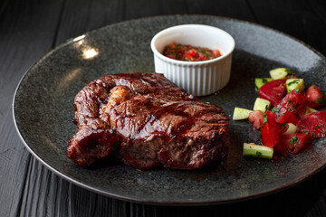 Meat steak with vegetables and sauce, on a dark plate, on a black background