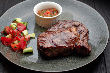 Meat steak with vegetables and sauce, on a light plate, on a black background