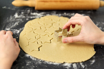 cooking food and culinary concept - close up of hands cutting shortcrust pastry dough with star...