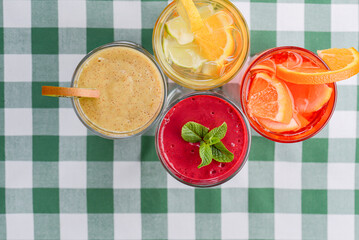 Four tropical mixed drinks, berries, orange and kiwi fruit cocktails served on green plaid tablecloth.