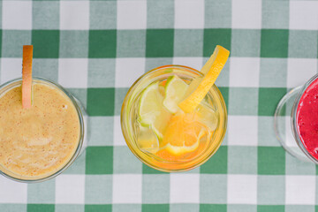 Three tropical mixed drinks, berries, orange and kiwi fruit cocktails served on green plaid tablecloth.