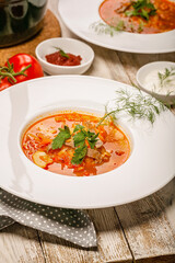 Close-up plate cabbage soup with beef, fresh tomatoes and herbs on a light wooden background. Vertical shot