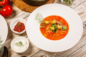 Close-up plate of soup with cabbage, beef, fresh tomatoes and herbs on a light wooden background.