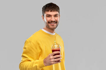 drinks and people concept - happy smiling young man holding tomato juice in takeaway plastic cup...
