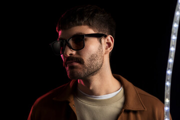 Obraz premium leisure, clubbing and nightlife concept - young man in sunglasses ain dark room over ultra violet neon lights at night club