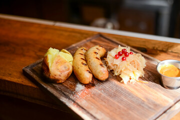 Baked potato with sausages and cabagge salad with sauce served on a wooden cutting board in a restaurant or cafe.