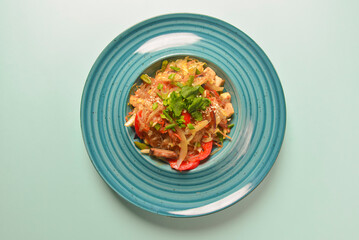 Plate of Asian chicken salad with rice noodles and sesame seeds served in a blue plate over blue mint background.