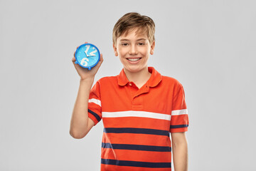 childhood, fashion and people concept - portrait of happy smiling boy in red polo t-shirt with alarm clock over grey background