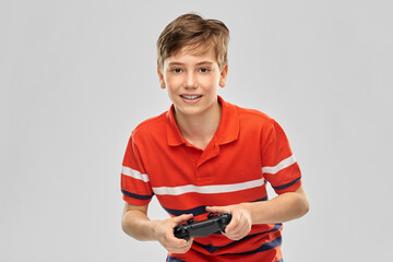 childhood, fashion and people concept - portrait of happy smiling boy in red polo t-shirt with gamepad playing video game over grey background © Syda Productions